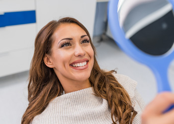 Woman smiling at reflection in handheld mirror