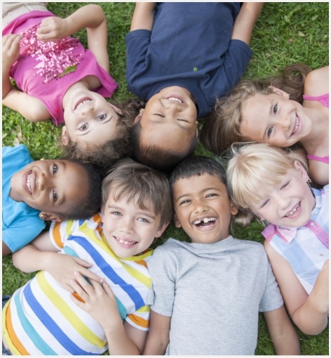 Group of smiling kids laying in grass with their heads forming a circle