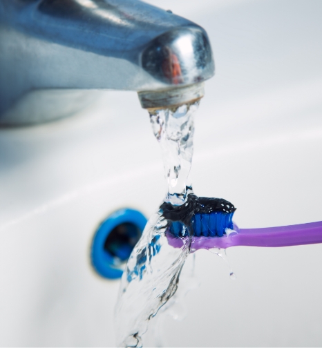 Toothbrush with black toothpaste being rinsed in sink