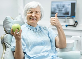 Patient smiling while holding an apple in the dentist’s chair