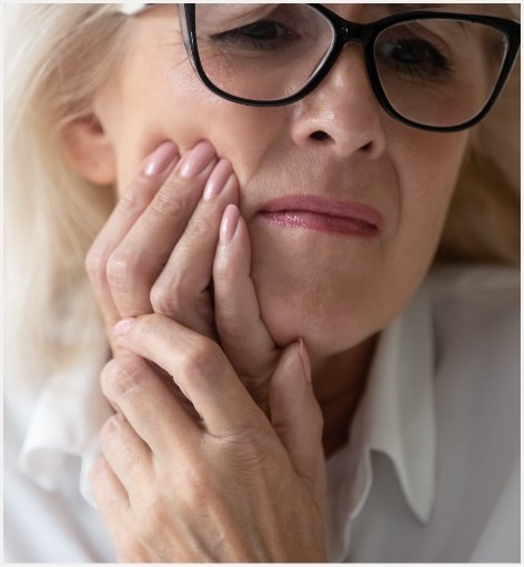 Woman holding her cheek in pain needing emergency dentist in Hayward