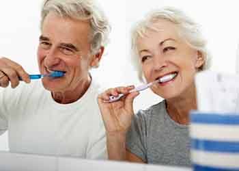 a mature couple smiling and brushing their teeth