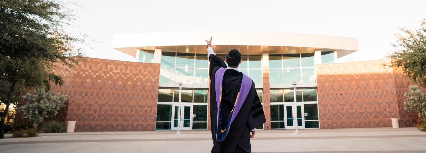 Doctor Diep in graduation cap and gown standing in front of college building with his back to the camera