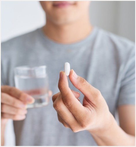 Man taking white pill with glass of water